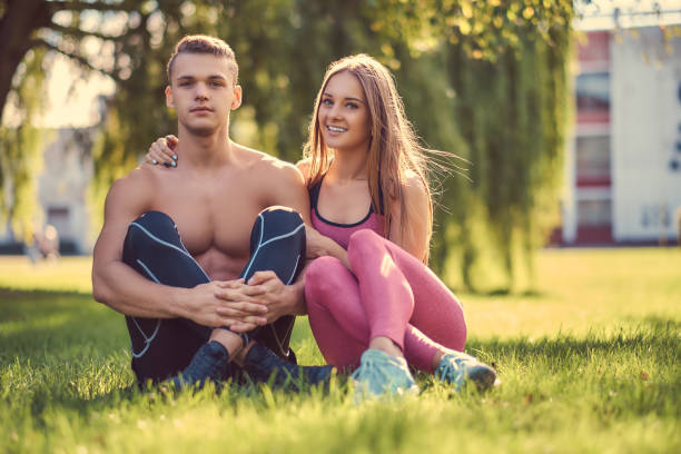 健康的なライフスタイルコンセプト。緑の草の上に座っている間幸せな若いフィットネスカップル抱きしめる。 - free your mind 写真 ストックフォトと画像