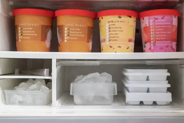 Photo of Full of bucket container ice creams flavors and ice cubes in freezer.