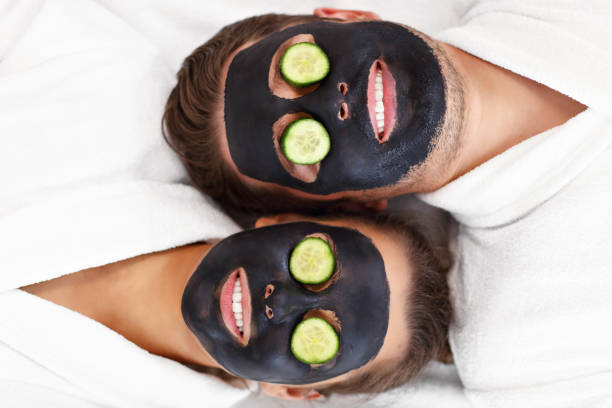 pareja feliz teniendo facial en salón de spa - facial mask spa treatment cucumber human face fotografías e imágenes de stock