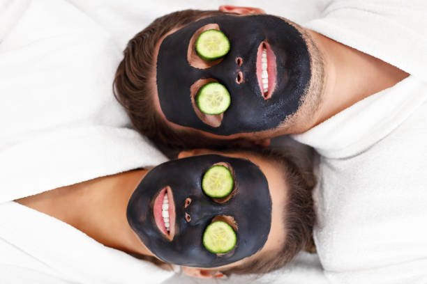 couples heureux ayant le soin du visage dans le salon de spa - cucumber facial mask human face women photos et images de collection