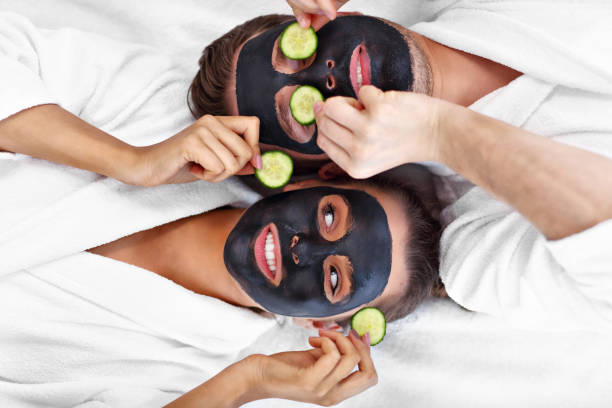 happy couple having facial in spa salon - facial mask spa treatment cucumber human face imagens e fotografias de stock