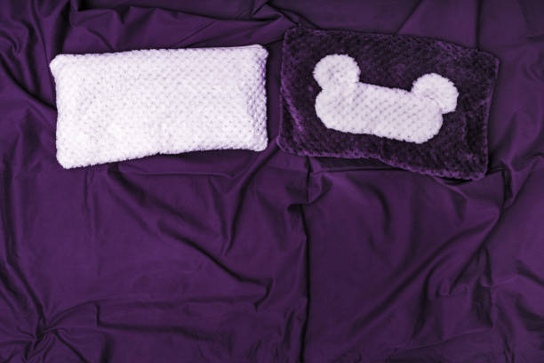 istock Soft pillow and sleep mask on dark violet crumpled sheet.  Top  view. Flat lay. 1138203167