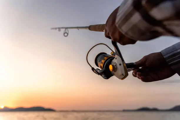 Fishing on the lake at sunset. Closeup spinning in the male hand, Fishing background.