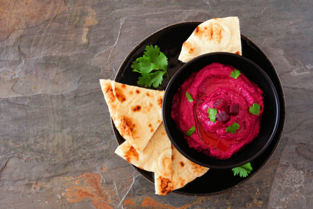 Beet hummus dip with pita bread on a black plate, above view on a dark background