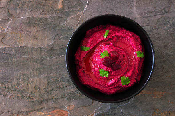 Beet hummus dip in a black bowl, above view on a dark background