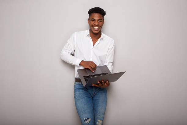 istock happy young black man holding laptop computer by gray wall 1138213115