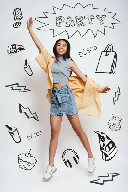 Going crazy! Happyyoung asian woman smiling and jumping against grey background with party theme doodles on it. Happiness concept. Party concept. Disco