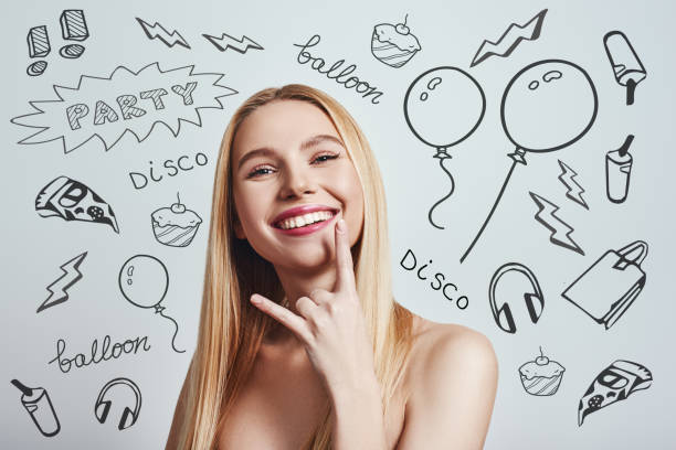 istock Feeling free. Cute blonde young woman gesturing and smiling at camera while standing against grey background with party theme doodles on it. Having fun. 1138220377