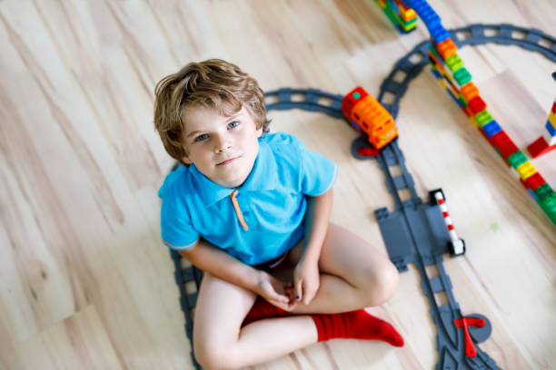 istock Adorable little blond kid boy playing with colorful plastic blocks and creating train station. Child having fun with building railway toys at home 1138220494