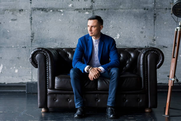istock Beautiful elegant fashionable young man in a blue jacket sits on a leather sofa 1138220559