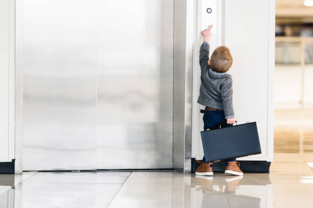 Reaching New Heights Little boy (preschool aged) in businessman attire, carrying a briefcase, on tippy toes to try and reach the elevator button. short stature stock pictures, royalty-free photos & images