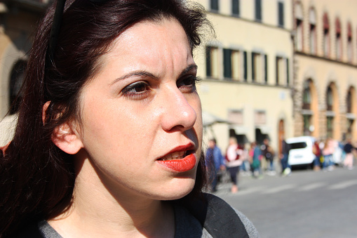 face of girl tourist traveling around the world with backpacking. light Caucasian skin, long brown hair, red lipstick on the lips and a look through the streets of Tuscany
