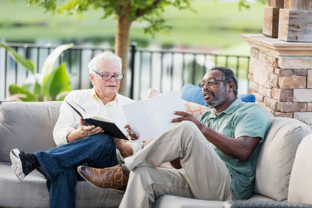 istock Retired men sitting on patio reading books, conversing 1138224287