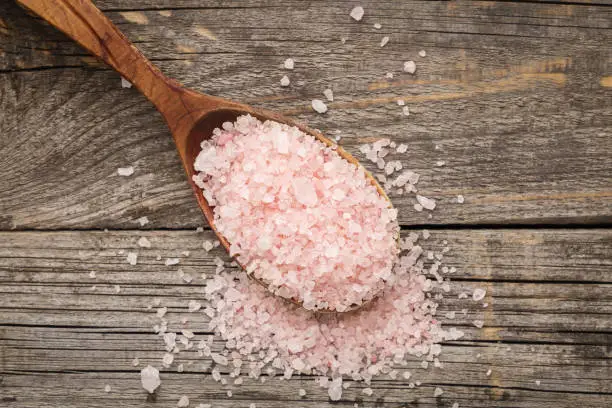 Pink salt in wooden spoon on wooden table. Top view