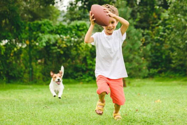 kid jugando fútbol americano listo para hacer touchdown y perro persiguiéndolo - dog lawn grass front or back yard fotografías e imágenes de stock