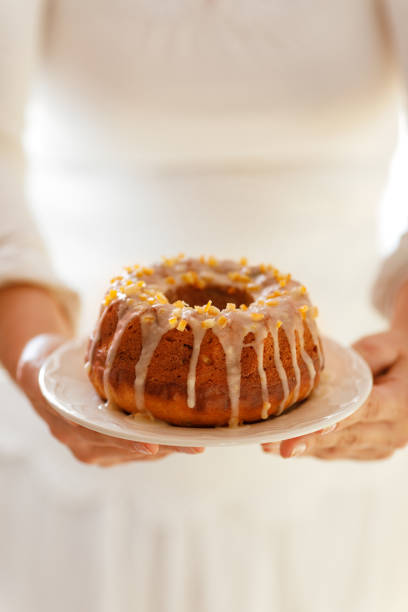 Easter Yeast cake on a white plate held by female hands, when served to the table. Traditional Easter cake with raisins and icing with candied orange peel
