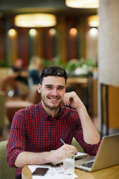 istock Cheerful confident handsome young man with eyeglasses on head sitting at table and looking at camera while preparing for informal meeting in cafe 1138230090