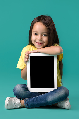 cute little child girl holding blank tablet computer on blue background