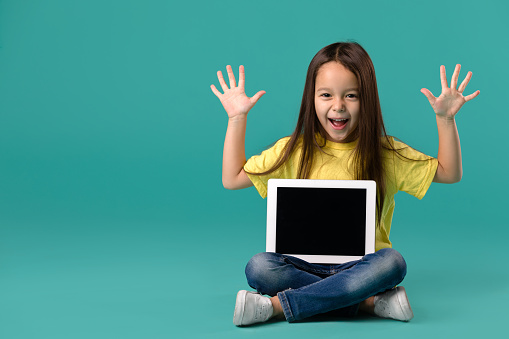 happy cute little child girl holding blank tablet computer on blue background