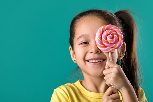 smiling cute little child girl with sweet candy lollipop isolated on blue background