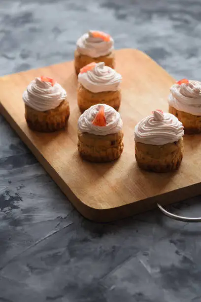 Homemade healthy sugar free sweets. Muffins with cream cheese and blood orange icing on cutting board on dark background copyspace