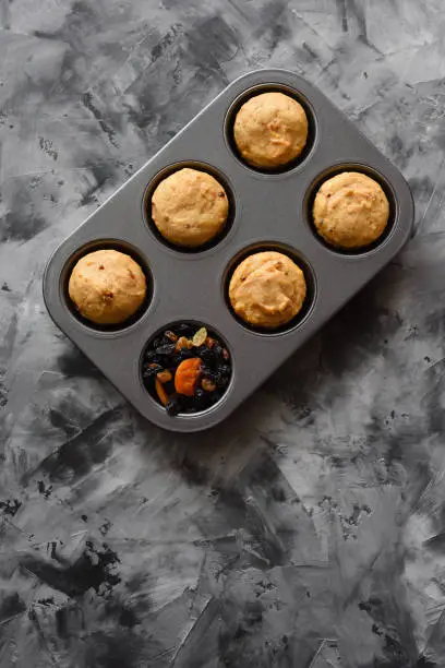 Homemade healthy imperfect sweets. Muffins with dried fruits in baking pan on dark background minimalist style top view copyspace
