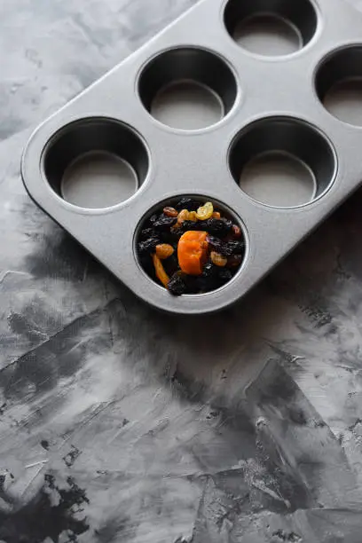 Concept of healthy clean eating. Dried apricots and raisins in empty muffin baking pan on gray background top view copyspace