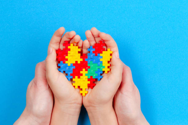 manos de adultos y niños sosteniendo corazón colorido en fondo azul. el concepto de día mundial de concientización del autismo - autismo fotografías e imágenes de stock