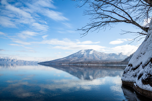 on a calm winter morning in February, the shallow water of Lake Shikotsu reflects the mountains and clouds above.