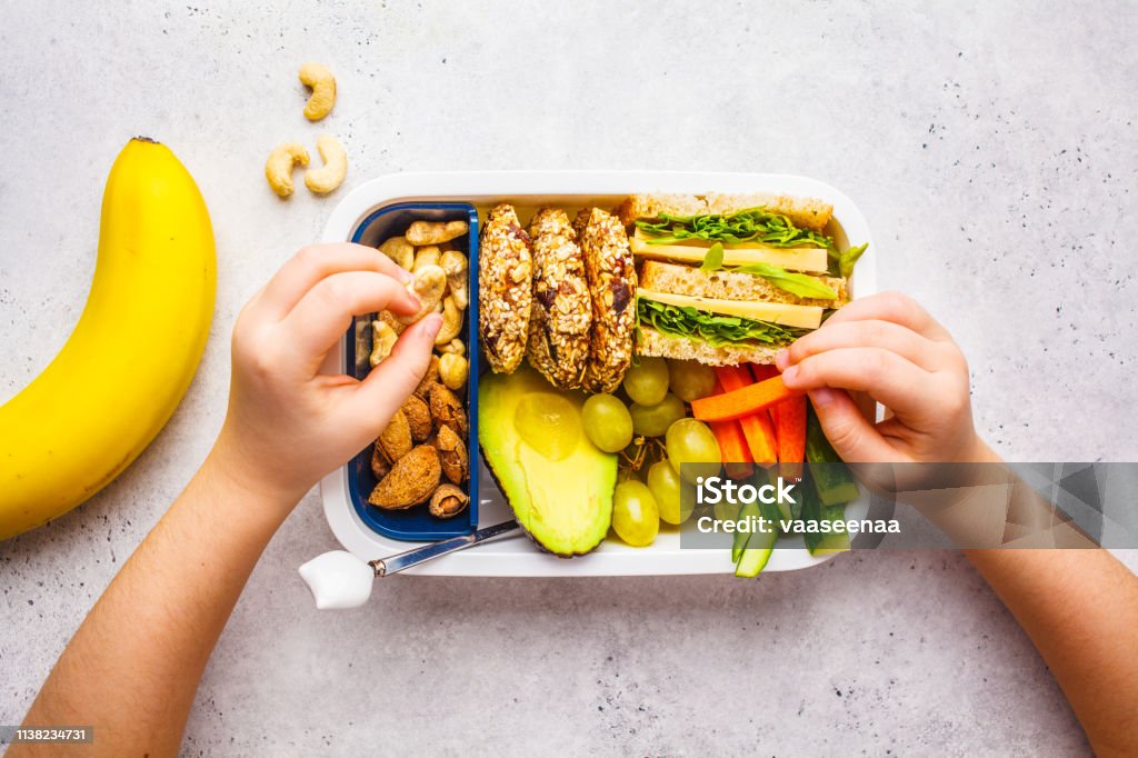 School healthy lunch box with sandwich, cookies, fruits and avocado on white background. School healthy lunch box with sandwich, cookies, nuts, fruits and avocado on a white background. Child Stock Photo