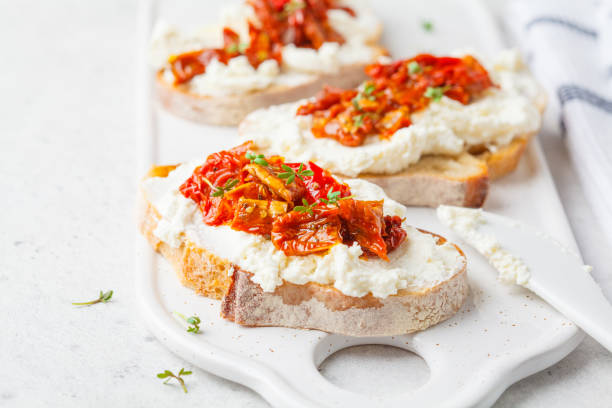 sándwiches de ricotta y tomates secados al sol en pizarra blanca. - bruschetta cutting board italy olive oil fotografías e imágenes de stock