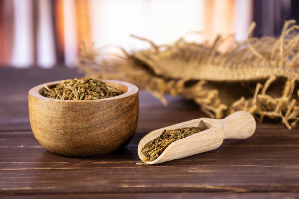 Roman caraway cumin with curtains Lot of whole roman caraway seeds in a scoop with wooden bowl with silk curtains behind carum carvi stock pictures, royalty-free photos & images