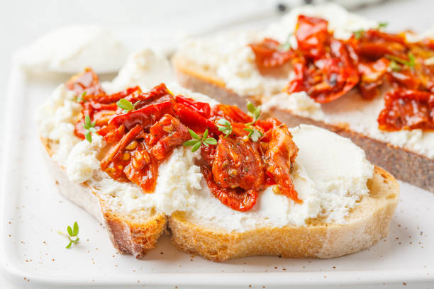 ricota e sanduíches secados sol dos tomates na placa branca. - bruschetta cutting board italy olive oil - fotografias e filmes do acervo