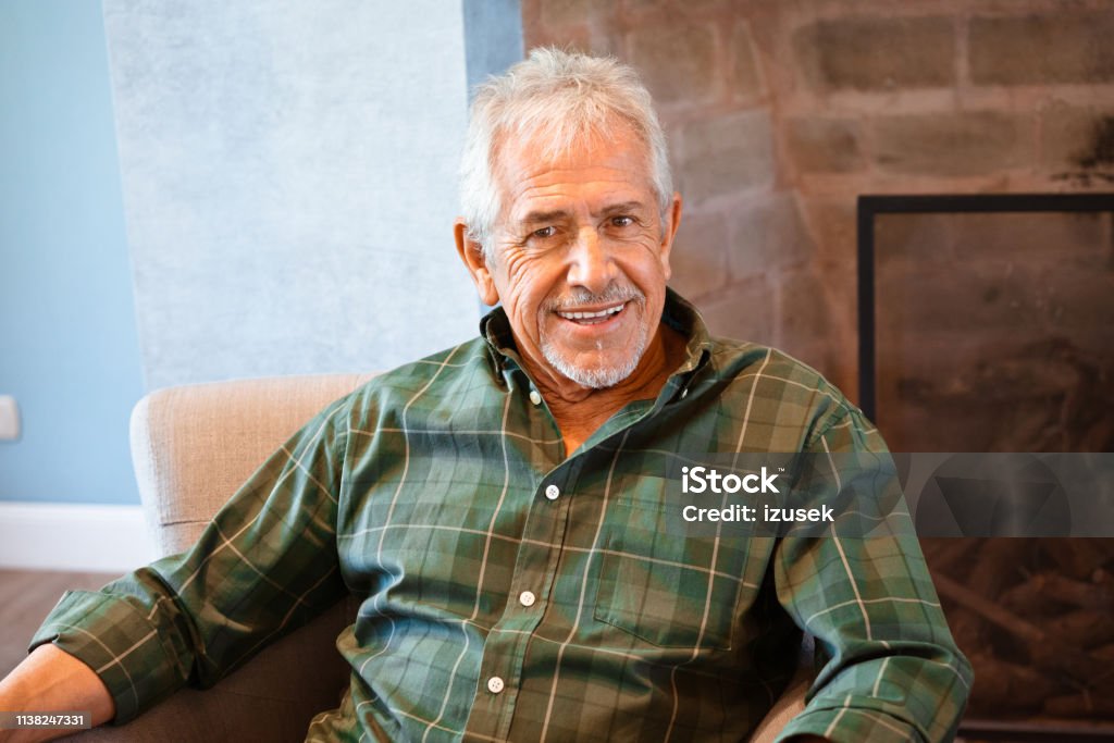 Portrait of happy elderly man at nursing home Portrait of smiling elderly male. Senior man is sitting on armchair at nursing home. He is wearing plaid shirt. Armchair Stock Photo