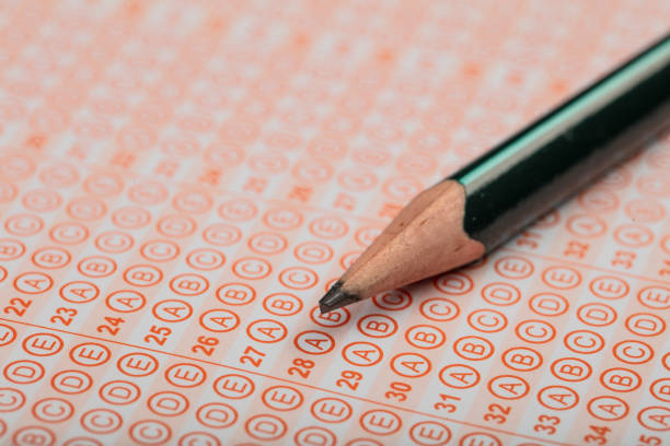 istock high school or university student hands taking exams, writing examination on paper answer sheet optical form of standardized test on desk doing final exam in classroom. Education literacy concept. 1138247414