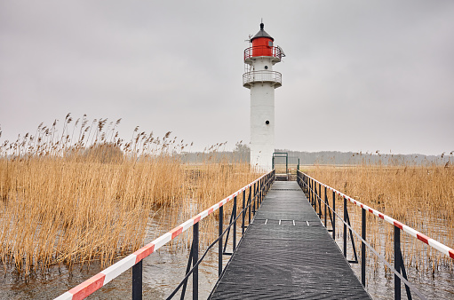 Inland waterway lighthouse seen from a steel pier on a cloudy day.