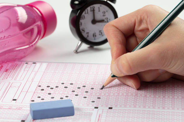 istock high school or university student hands taking exams, writing examination on paper answer sheet optical form of standardized test on desk doing final exam in classroom. Education literacy concept. 1138248453