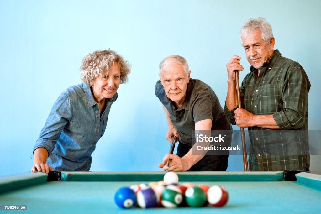 Senior male and female friends playing pool ball Male and female senior friends playing pool ball. Elderly men and woman are having fun together. They are at nursing home. Pool - Cue Sport Stock Photo