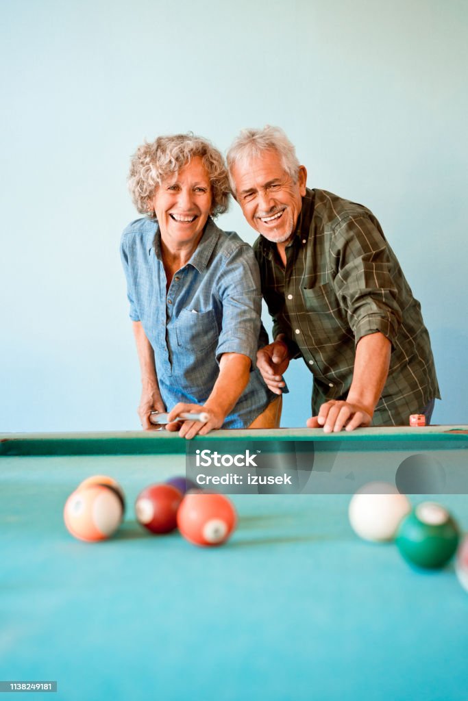 Happy senior friends playing pool ball together Happy senior friends playing pool ball. Elderly man and woman are enjoying at nursing home. They are having fun together. Pool - Cue Sport Stock Photo