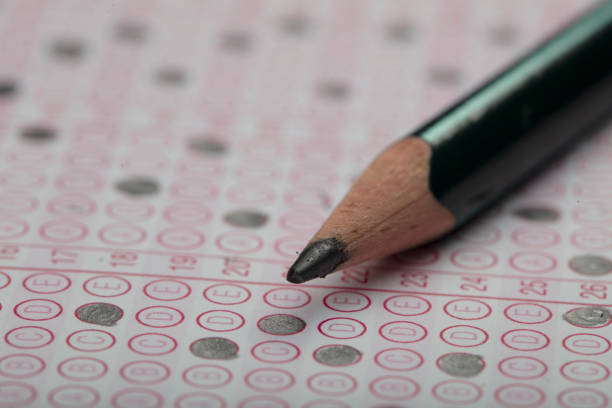 istock high school or university student hands taking exams, writing examination on paper answer sheet optical form of standardized test on desk doing final exam in classroom. Education literacy concept. 1138249793