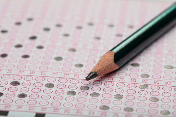 istock high school or university student hands taking exams, writing examination on paper answer sheet optical form of standardized test on desk doing final exam in classroom. Education literacy concept. 1138250098