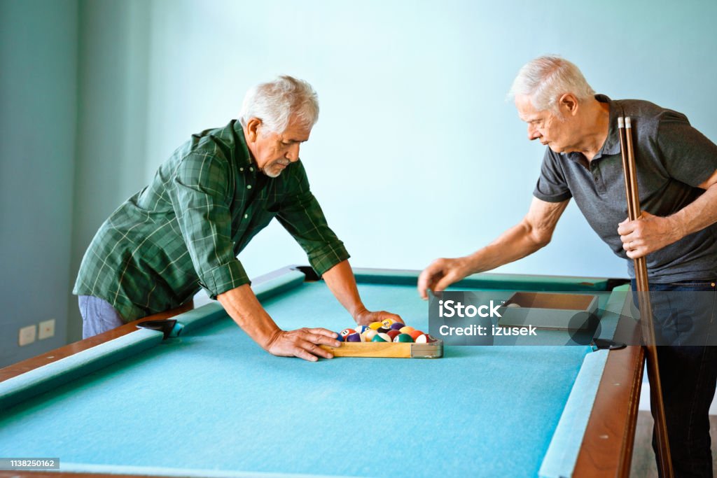 Senior friends arranging balls on pool table Male friends arranging balls on pool table. Elderly men having fun at nursing home. They are playing competitive sport. Pool - Cue Sport Stock Photo