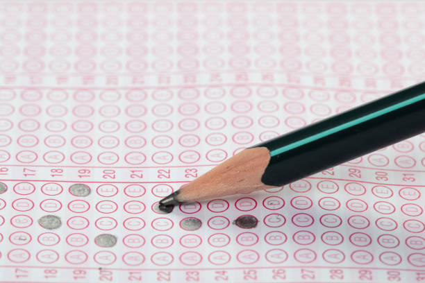 istock high school or university student hands taking exams, writing examination on paper answer sheet optical form of standardized test on desk doing final exam in classroom. Education literacy concept. 1138250733
