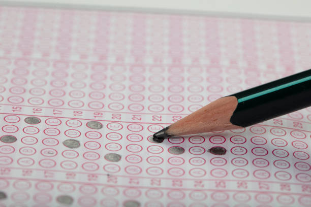 istock high school or university student hands taking exams, writing examination on paper answer sheet optical form of standardized test on desk doing final exam in classroom. Education literacy concept. 1138251803