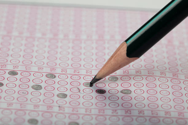 istock high school or university student hands taking exams, writing examination on paper answer sheet optical form of standardized test on desk doing final exam in classroom. Education literacy concept. 1138251957