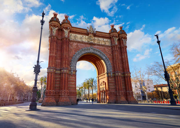 Sunrise at Triumphal Arch in Barcelona, Catalonia, Spain. Sunrise at Triumphal Arch in Barcelona, Catalonia, Spain. Arc de Triomf at boulevard street. Alley with tropical palm trees. Early morning landscape with shadows and blue sky with clouds. Famous panoramic country road single lane road sky stock pictures, royalty-free photos & images