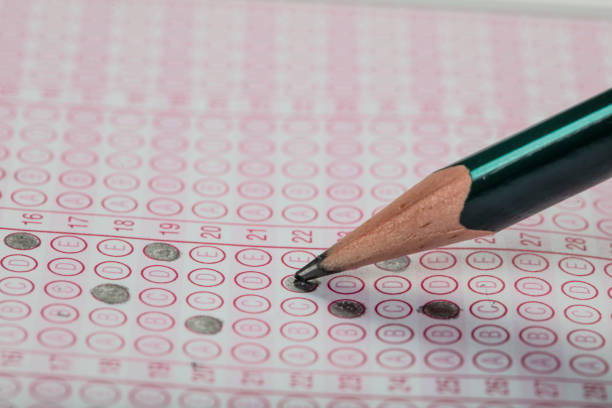 istock high school or university student hands taking exams, writing examination on paper answer sheet optical form of standardized test on desk doing final exam in classroom. Education literacy concept. 1138252264