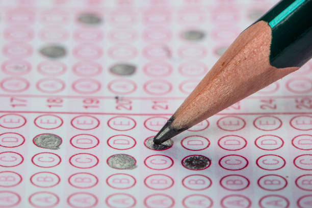 istock high school or university student hands taking exams, writing examination on paper answer sheet optical form of standardized test on desk doing final exam in classroom. Education literacy concept. 1138252400