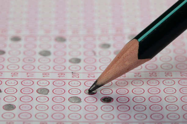 istock high school or university student hands taking exams, writing examination on paper answer sheet optical form of standardized test on desk doing final exam in classroom. Education literacy concept. 1138252558