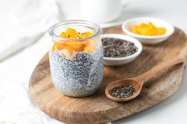 Chia pudding in glass jar with almond milk and mango on white background Chia pudding in glass jar with almond milk and mango on wooden cut board, white background - healthy superfood vegan, dairy free breakfast chia seed photos stock pictures, royalty-free photos & images
